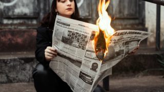 新聞が燃えている状態で新聞を読んでいる少女